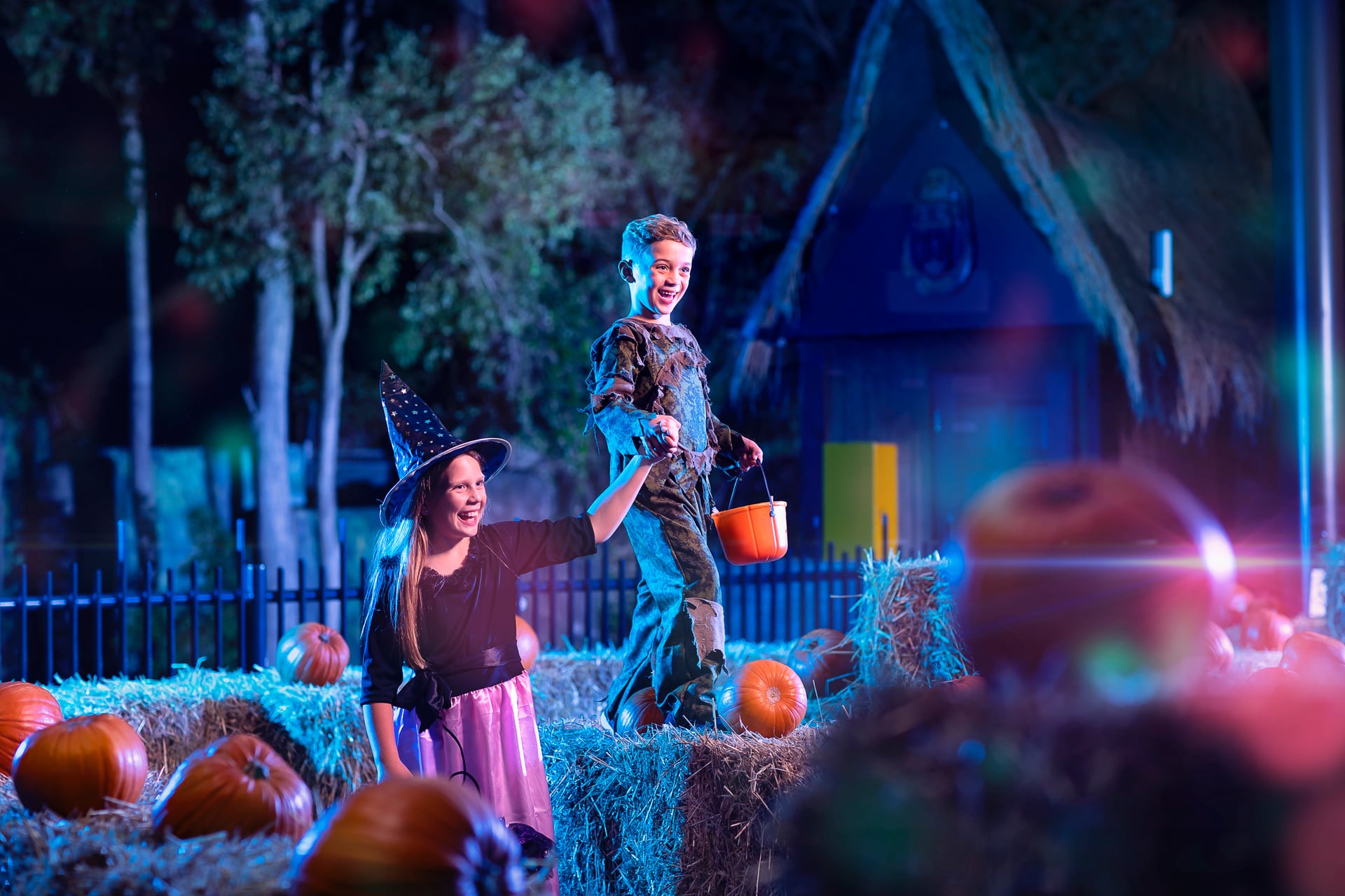 Two children dressed in Halloween costumes trick-or-treating among pumpkins and hay bales at Dreamworld’s Happy Halloween event.
